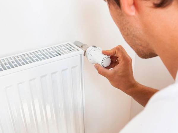 Une main règle le thermostat d’un radiateur