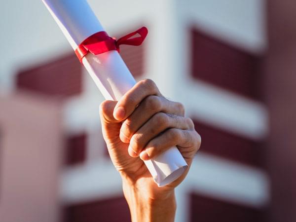 Une main tient un diplôme enroulé et lié par un ruban rouge
