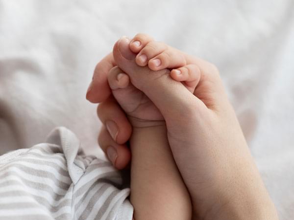 Main d’un bébé tenant le pouce de sa mère