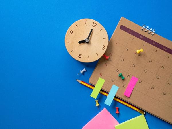 Pendule, calendrier, crayon, post it et punaises sur fond bleu